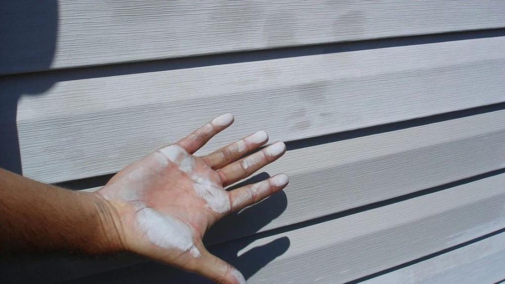 A hand covered in white chalky oxidation after touching faded vinyl siding
